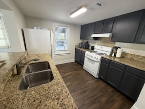 A kitchen with granite countertops, a double sink, a stove, and dark cabinetry. - The Downtown Cedar - walk to Government St & Washington (Ocean Springs)