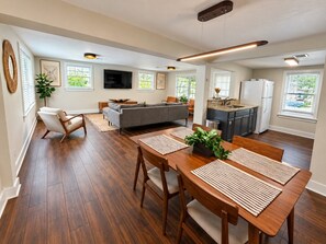 A modern kitchen with a built-in oven, a refrigerator, and a dining area with a wooden table and chairs. - The Downtown Cedar - walk to Government St & Washington (Ocean Springs)