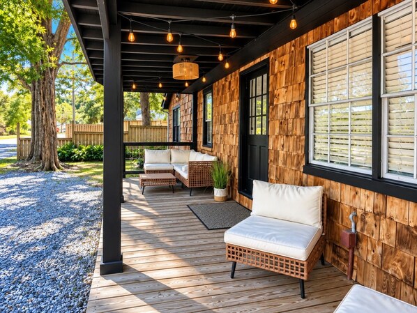 A covered outdoor seating area with wicker furniture and a wooden deck. - The Downtown Cedar - walk to Government St & Washington (Ocean Springs)