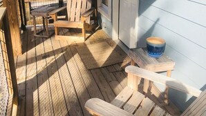 Una terraza de madera con sillas tipo Adirondack, una mesita y una puerta a un edificio.