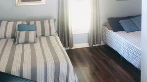 Un dormitorio con una cama, una cama individual, un ventilador de techo, aire acondicionado y una ventana con cortinas.