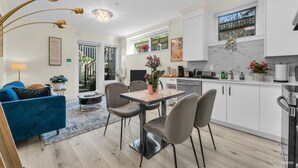 Uma cozinha moderna com armários brancos, bancada de mármore e um espaço de jantar com mesa e cadeiras.