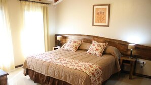 A bedroom with a large bed, two bedside tables, a nightstand, a framed picture on the wall, and a window with curtains. - Posada Del Jacarandá (Puerto Iguazu)