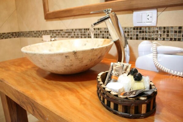 A bathroom with a large bowl sink, a faucet, a hairdryer, and a basket with toiletries.