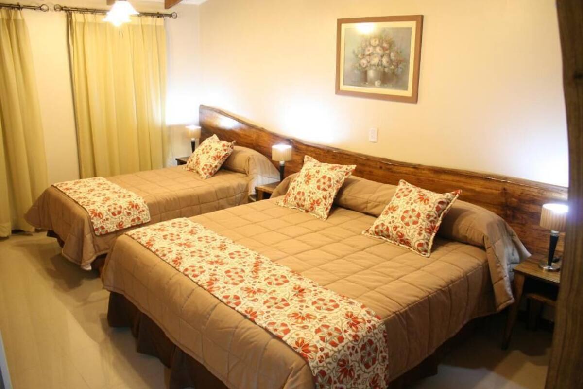 A double room with two beds, a wooden headboard, a painting on the wall, and a desk with a lamp.