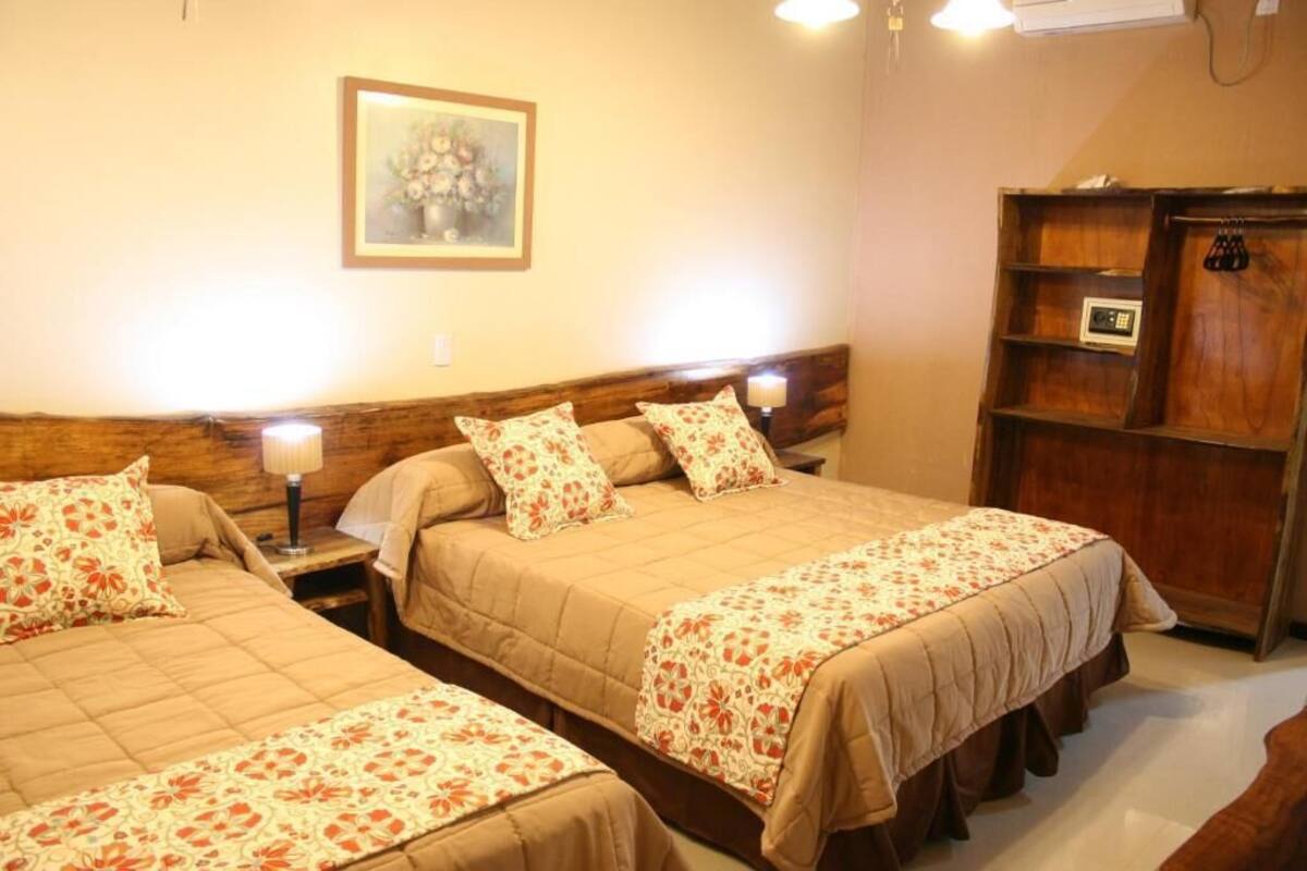 A hotel room with two beds, a wooden headboard, a nightstand with a lamp, a wooden wardrobe, and a framed picture on the wall.