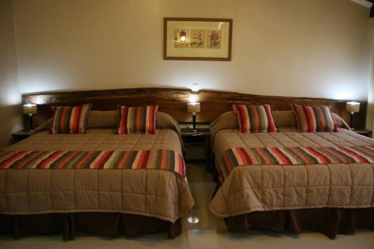A double room with two beds, each with a striped bedspread and matching pillows.