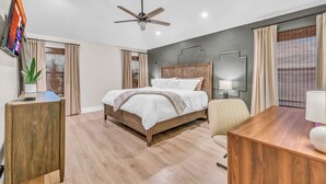 Une chambre d’hôtel moderne équipée d’un lit, d’un bureau, d’une chaise, d’un ventilateur de plafond et d’un téléviseur fixé au mur.