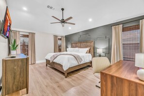 Une chambre d’hôtel moderne équipée d’un lit, d’un bureau, d’une chaise, d’un ventilateur de plafond et d’un téléviseur fixé au mur.