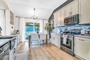 A modern kitchen with stainless steel appliances, a dining area with chairs, and a view to the outside. - Backyard Paradise • Hot Tub • Fire Pit • 13 guests (McKinney)