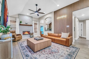 A modern living room with a fireplace, leather sofa, wooden coffee table, and a ceiling fan. - Backyard Paradise • Hot Tub • Fire Pit • 13 guests (McKinney)