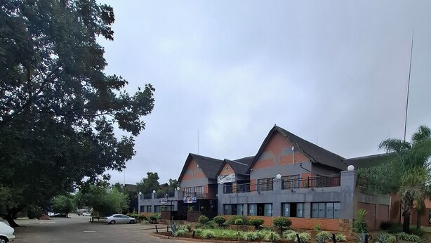 A building with a flat roof, multiple windows, and a paved area in front. - Charming 1-bedroom apartment in Bloemfontein perfect for your stay (Bloemfontein)