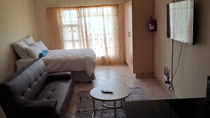 A room with a bed, a sofa, a small table, a TV, and a fire extinguisher. - Charming 1-bedroom apartment in Bloemfontein perfect for your stay (Bloemfontein)
