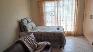 A bedroom with a bed, a sofa, a round coffee table, and a wardrobe. - Charming 1-bedroom apartment in Bloemfontein perfect for your stay (Bloemfontein)