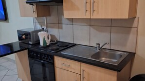 A kitchen with wooden cabinets, a stove, a microwave, and a sink. - Charming 1-bedroom apartment in Bloemfontein perfect for your stay (Bloemfontein)