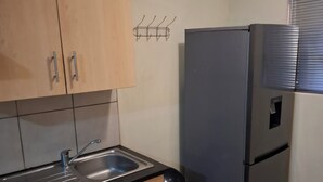A kitchen with wooden cabinets, a stainless steel sink, a refrigerator, and a trash bin. - Charming 1-bedroom apartment in Bloemfontein perfect for your stay (Bloemfontein)