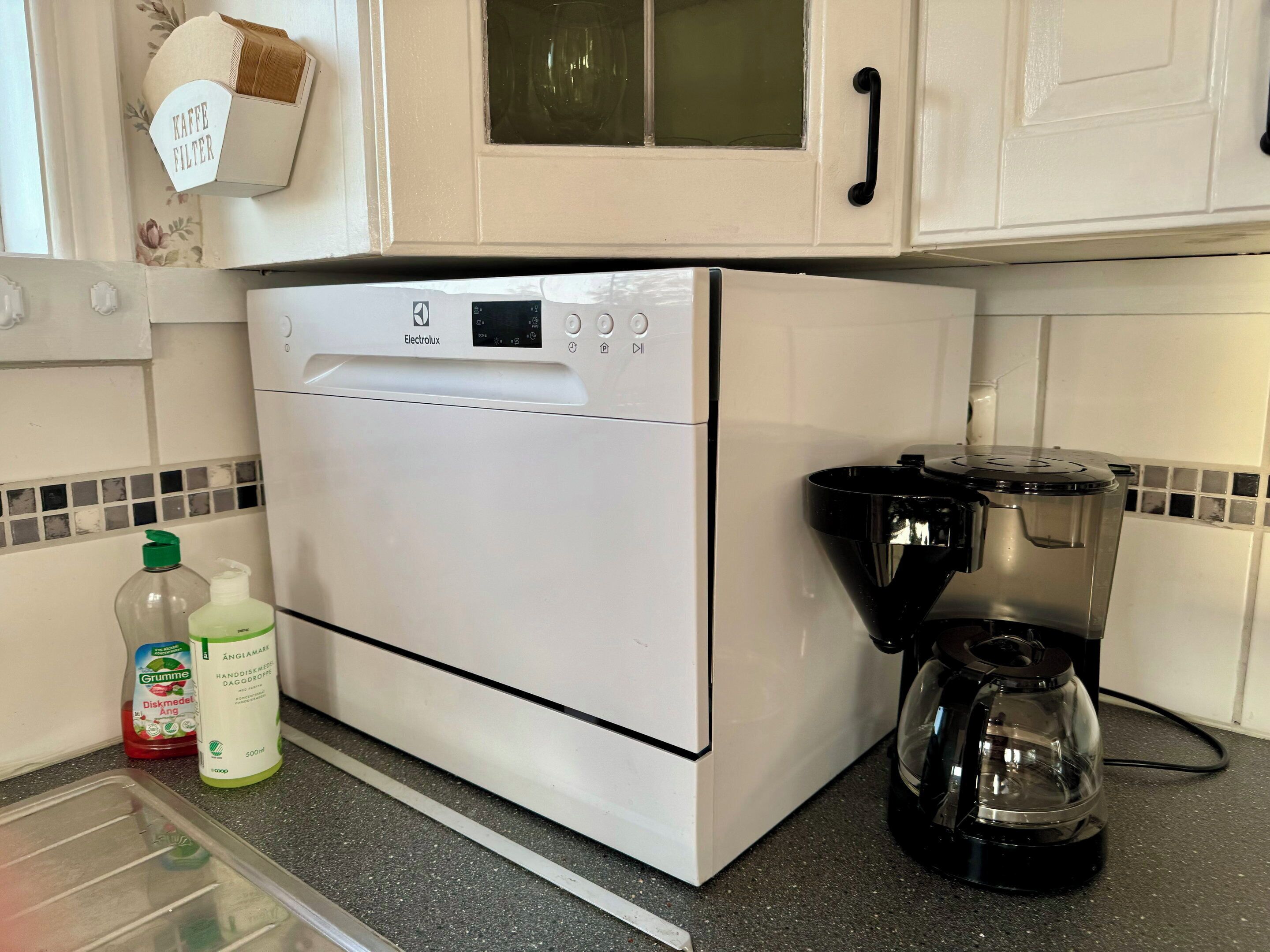 A kitchen with a white appliance, a coffee maker, and two bottles on the counter.