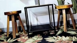 Una habitación con alfombra estampada, un objeto de marco negro en el centro y dos taburetes de madera.