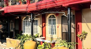 A red and beige building with arched windows, outdoor seating, and potted plants.