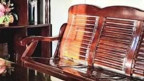 Un banco de madera con respaldo de listones, colocado junto a una mesa de vidrio con un arreglo floral.