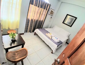 Une chambre dâhĂŽtel avec un lit, une petite table sur laquelle est posĂ©e une plante, une chaise, un banc en bois et une porte.