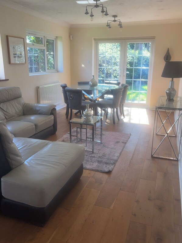 A living room with a glass-top dining table, leather sofas, a coffee table, and a radiator.