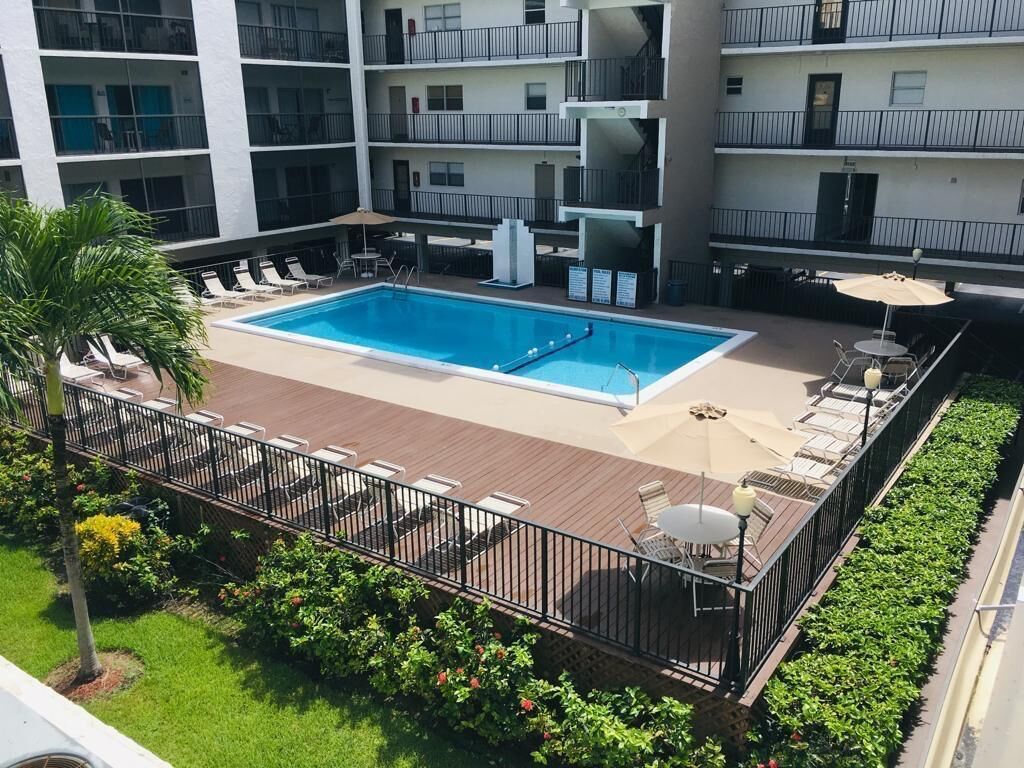 Una piscina sul tetto con poltrone prendisole, un tavolo con ombrellone e vista sui balconi dell'edificio.