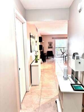 A modern living room with a sofa, a coffee table, and a TV. There is a balcony with a railing and a view of the outside. - Beach Apartment Sunny Isles Steps from the Beach (Sunny Isles Beach)