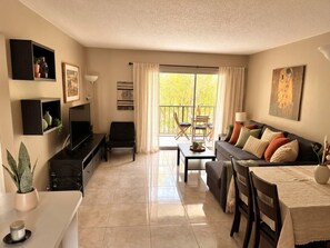 A living room with a sofa, a coffee table, a TV, and a dining area with chairs and a table. - Sunny Isles Beachfront Condo, Just Steps from the Beach (Sunny Isles Beach)