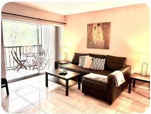 A living room with a sofa, coffee table, and chairs, a balcony with a table and chairs, and a painting on the wall. - Beach Apartment Sunny Isles Steps from the Beach (Sunny Isles Beach)