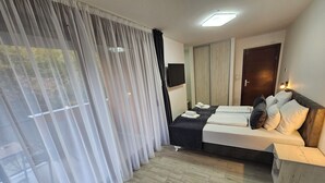 A hotel room with a bed, a TV, a wardrobe, and a window with sheer curtains. - 1BDR apartment, shared pool, kitchen, balcony, C21 (Sarajevo)