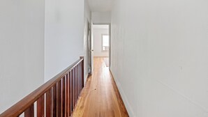 Un couloir étroit avec un plancher en bois, des murs blancs et une rambarde en bois.