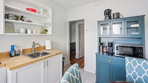 Une cuisine avec des meubles blancs, un plan de travail en bois, un évier et un meuble bleu contenant un four à micro-ondes.