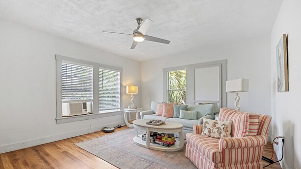 Un salon avec un ventilateur de plafond, une table basse ronde, un fauteuil à rayures, un canapé et un tapis.
