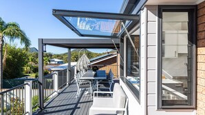 Un balcon doté d’une paroi vitrée, une table, des chaises et une vue sur une montagne et des maisons.
