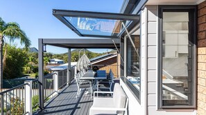 Ein Balkon mit Glasveranda, Tisch, Stühlen und Blick auf einen Berg und Häuser.