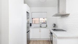 Eine kleine Küche mit weißen Schränken, einem Fenster, einer Edelstahlspüle und einem eingebauten Backofen.