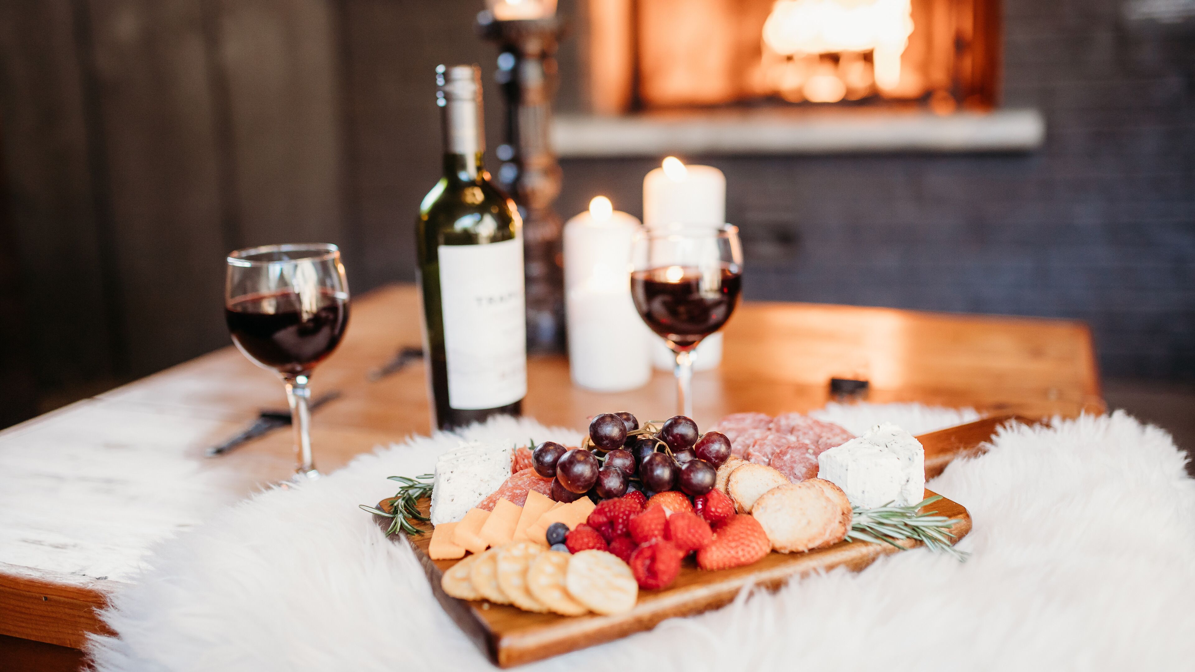Une table en bois avec une planche à fromage, des raisins, des fraises et une bouteille de vin.