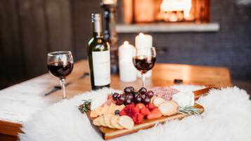 Une table en bois avec une planche à fromage, des raisins, des fraises et une bouteille de vin.