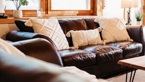 A brown leather sofa with two white throw pillows, a small table, and a window with a view. - Stunning Chalet at Whispering Springs (Grafton)