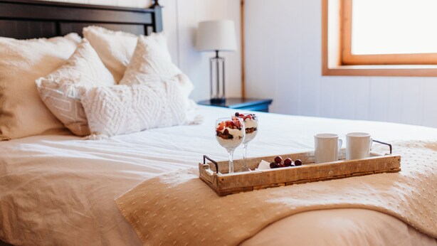 A neatly made bed with a tray of dessert and two cups, a bedside table with a lamp, and a framed picture on the wall. - Stunning Chalet at Whispering Springs (Grafton)