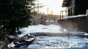A hot tub with a wooden deck, surrounded by snow and trees. - Stunning Chalet at Whispering Springs (Grafton)