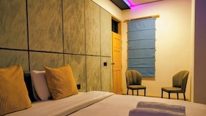 Habitación de hotel con cama, dos sillas, ventana con cortinas y armario de madera.