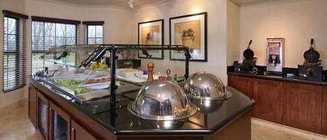 A buffet area with a glass display case, a coffee machine, and a fruit display.