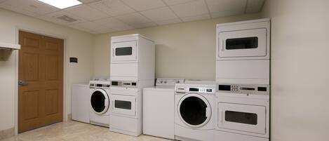 A laundry room with stacked washers and dryers, a wooden door, and a vent on the ceiling.