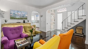 Ein modernes Wohnzimmer mit einer Couch, Sesseln, einem Couchtisch und einer Treppe, die eine weitere Ebene hinaufführt.