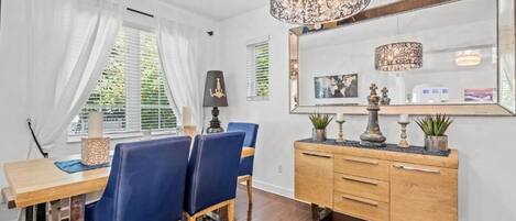 Een eetgedeelte met een houten tafel, blauwe stoelen, een houten kast en een grote spiegel.