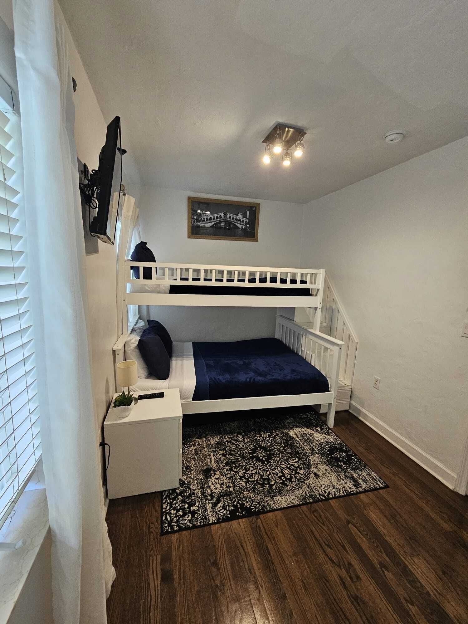 A bunk bed room with a small desk, a framed picture on the wall, and a patterned rug.