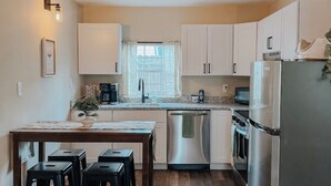 A modern kitchen with white cabinets, a stainless steel refrigerator, a dishwasher, and a dining area with stools. - Charming 3BR / Close to Downtown / Pet Friendly (Panama City)