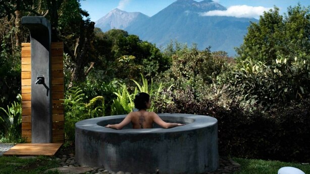 Uma pessoa relaxando em uma banheira de hidromassagem com vista para as montanhas.